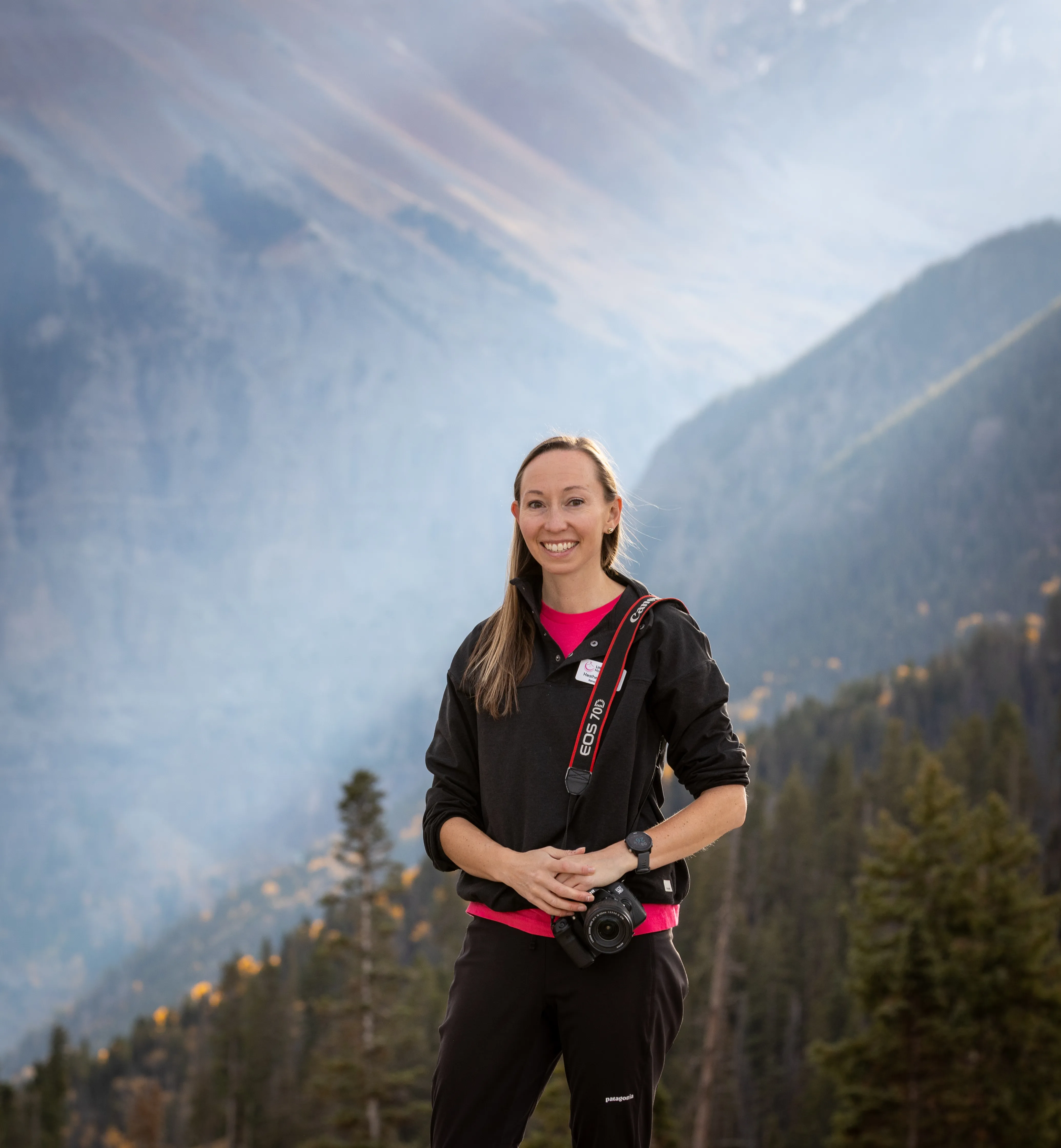 Heather Durosko standing with a camera in a mountain valley