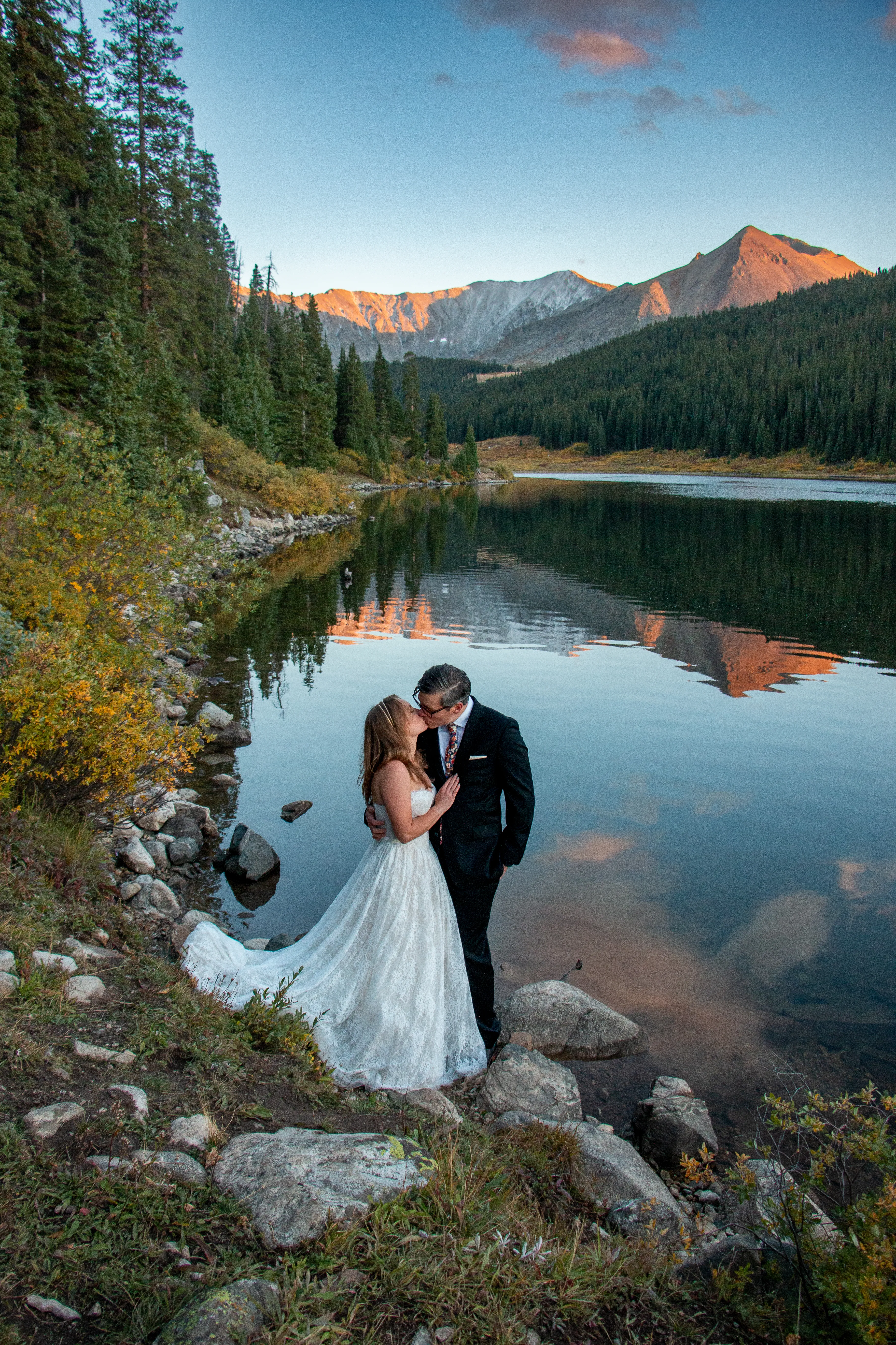 Bride and groom kissing beside a calm Colorado alpine lake